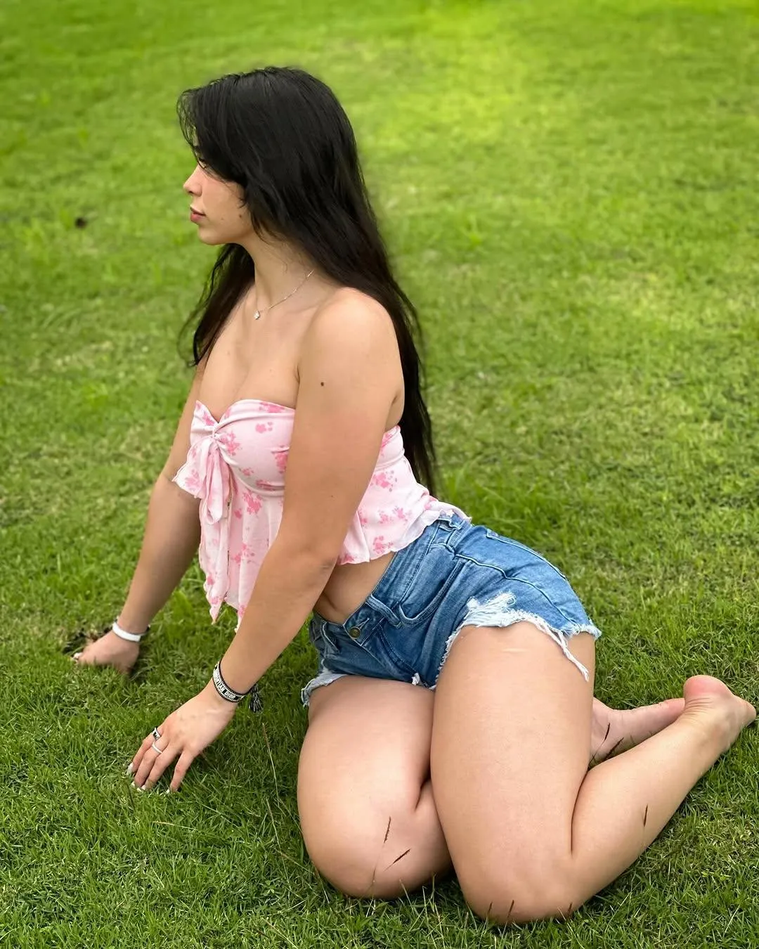 Girl in a Pink Top And Denim Shorts Kneels on Green Grass