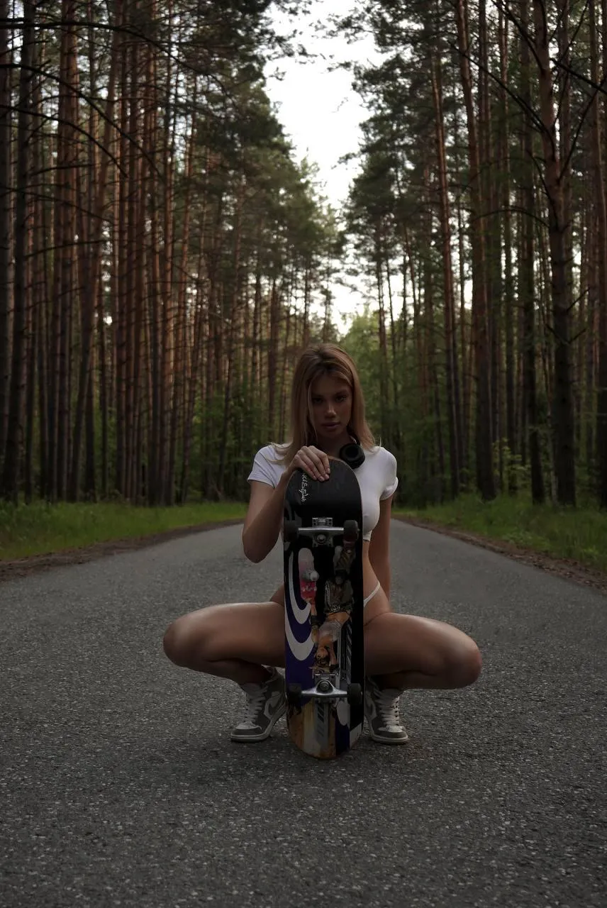 Girl Sitting with Skateboard in the Middle of a Forest Road