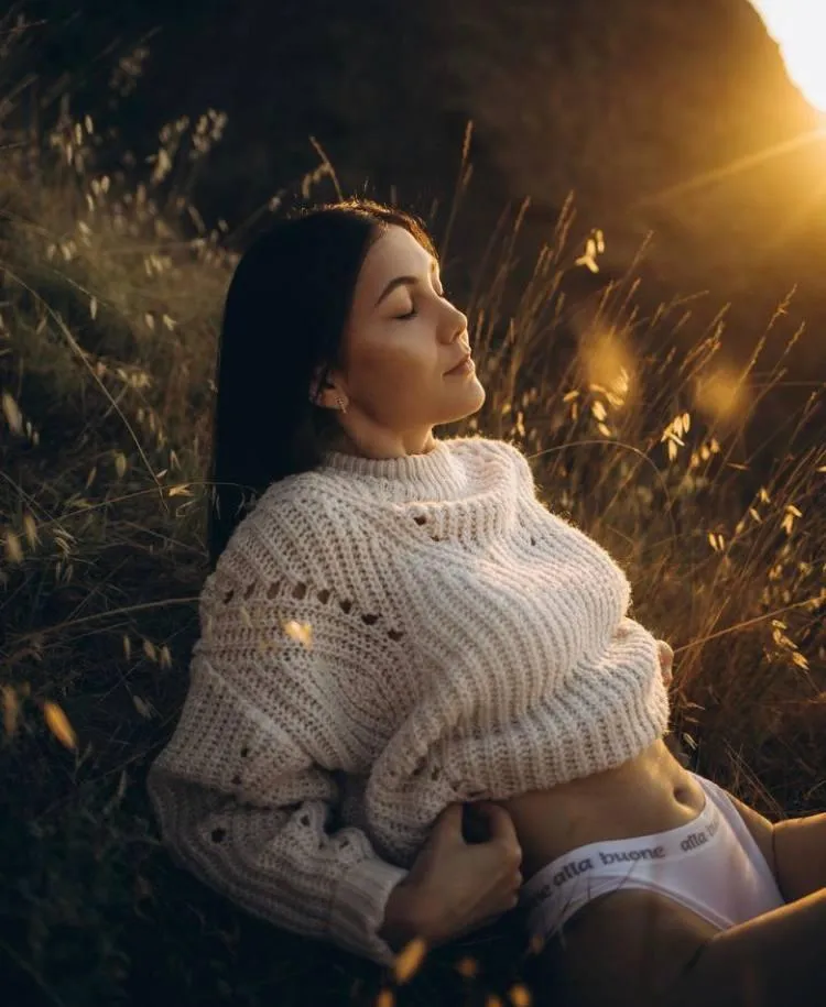 Golden portrait of woman in white sweater lying in the grass