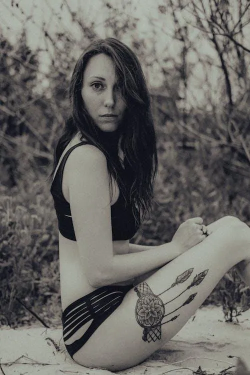 Grayscale image of a tattooed woman sitting on the beach sand