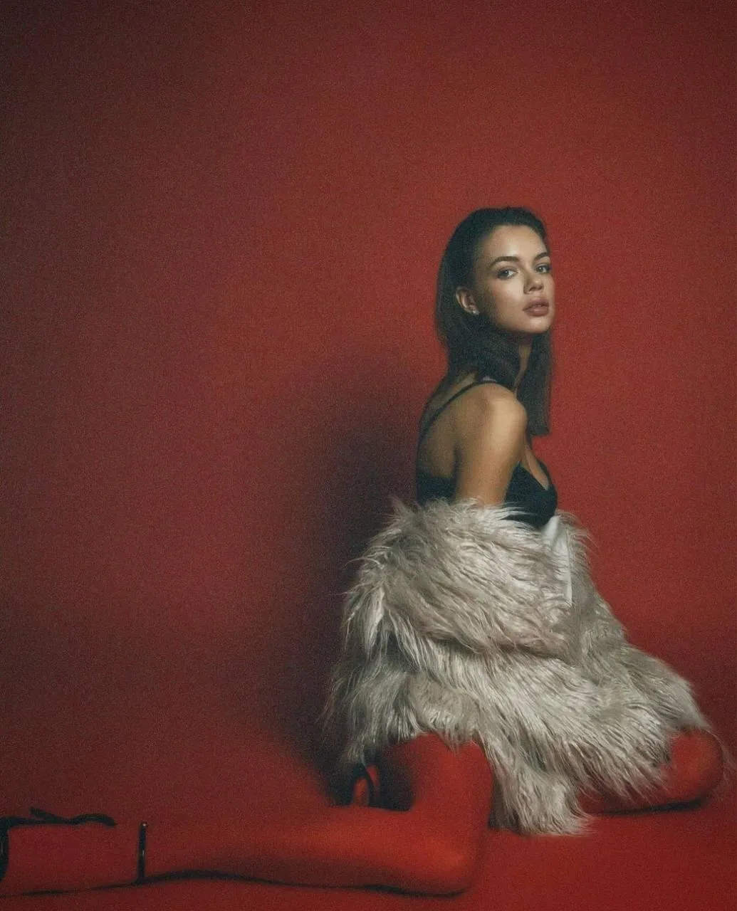 Model Wearing a Fur Coat Posing Against a Deep Red Backdrop