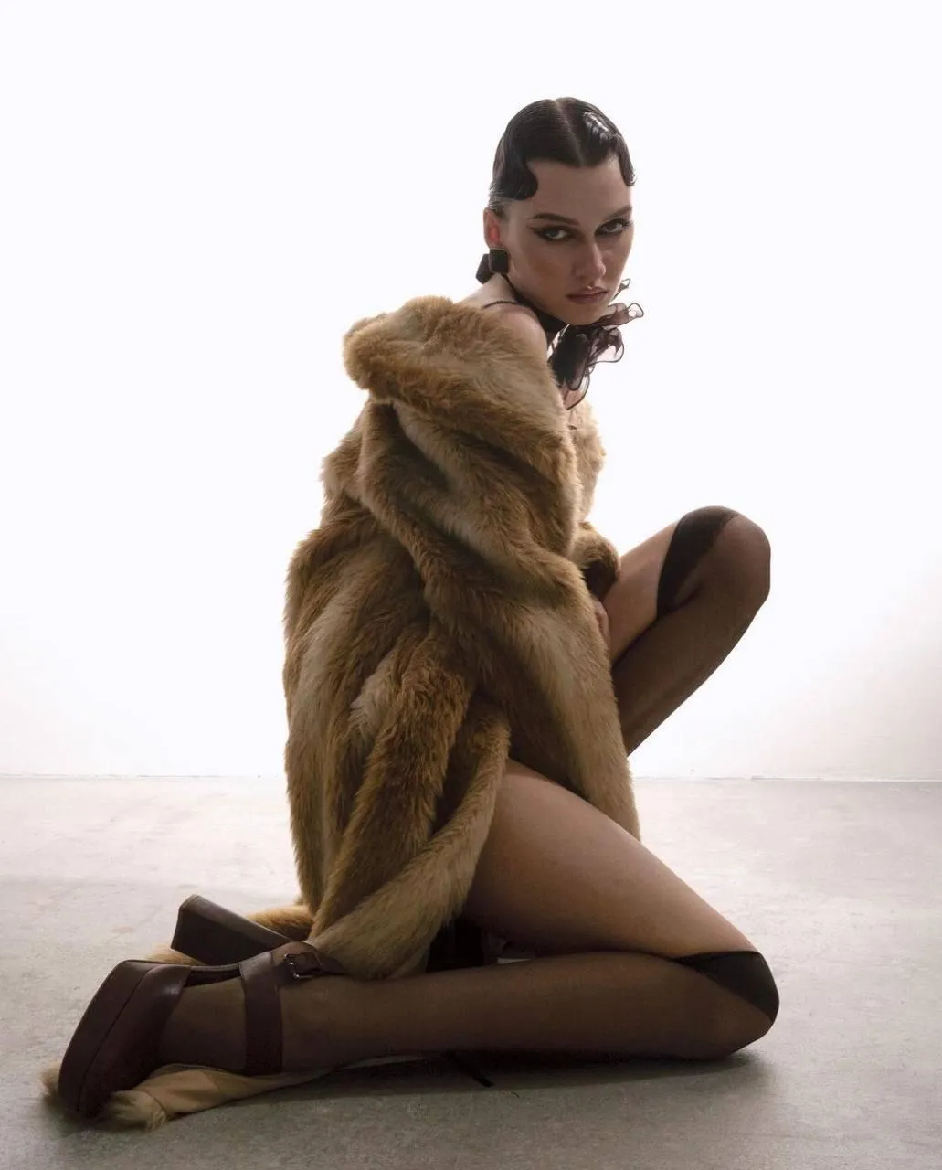 Model wearing a fur coat seated on floor with moody lighting