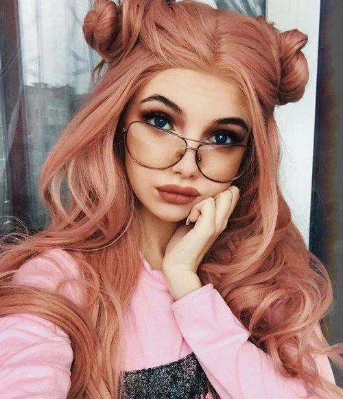 Playful woman with pink hair and glasses posing indoors