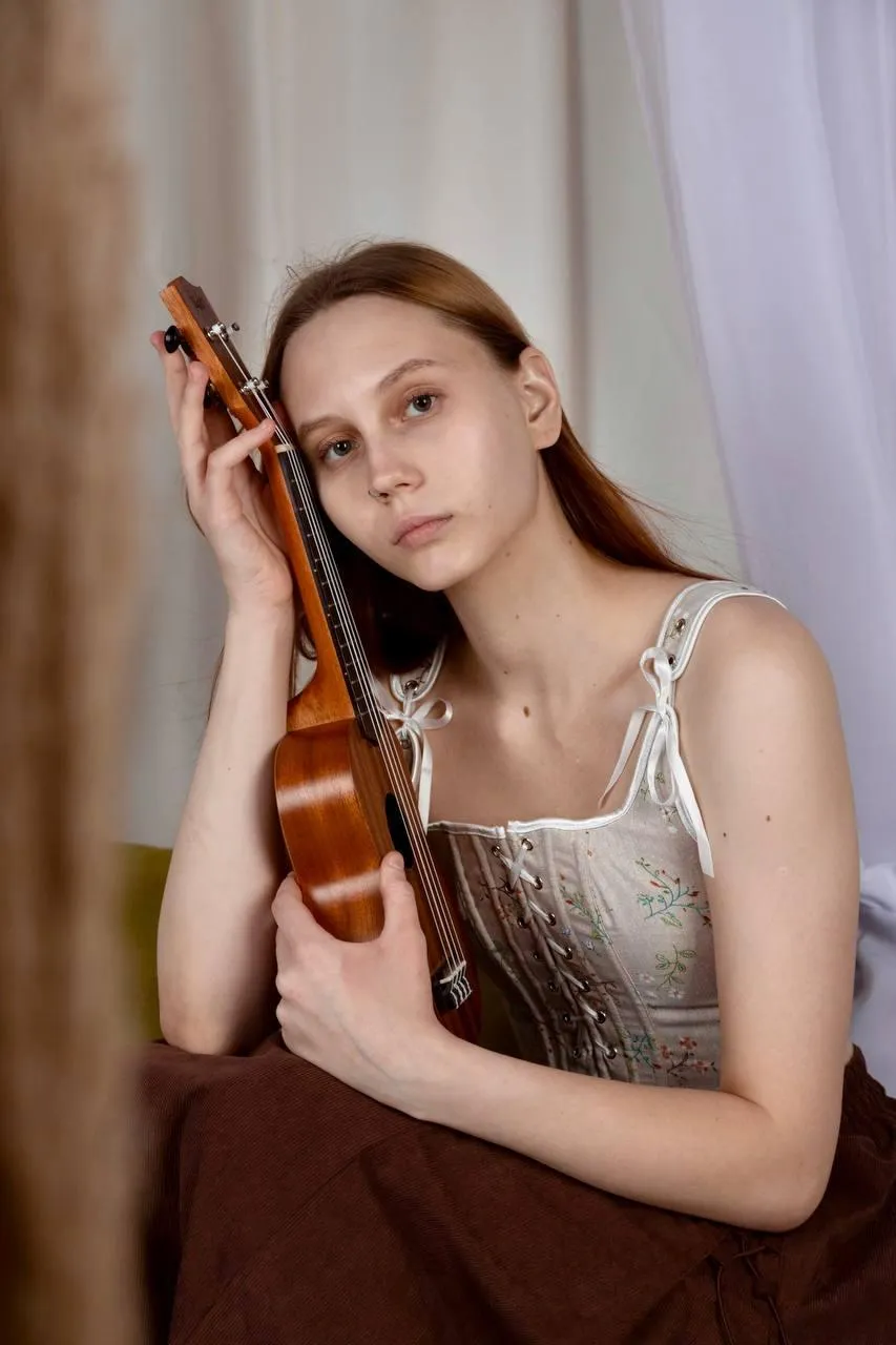 Seated woman holding a violin beside a brown curtain image