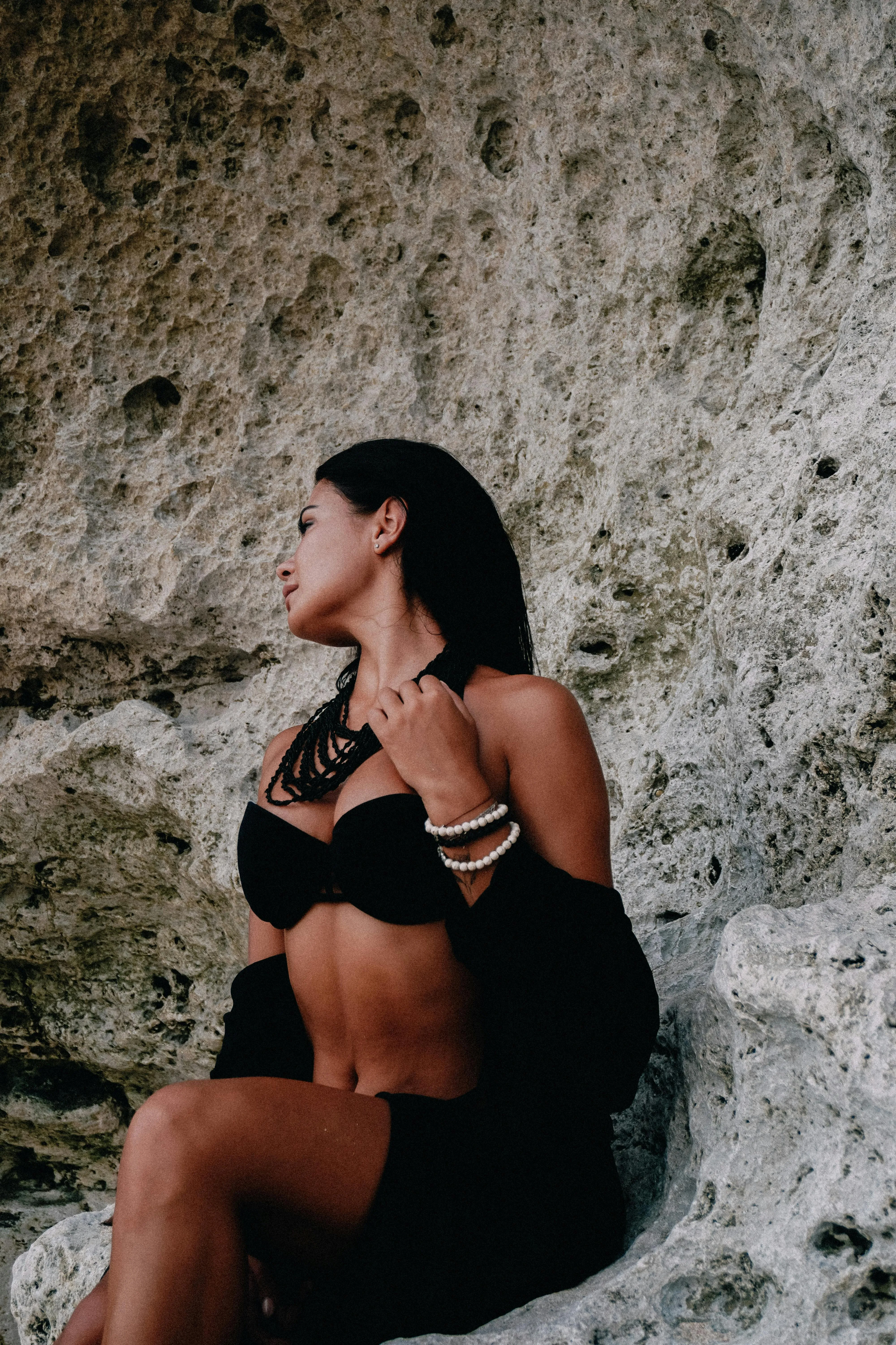 Seated Woman in Black Lingerie Near the Rocky Beach Wall
