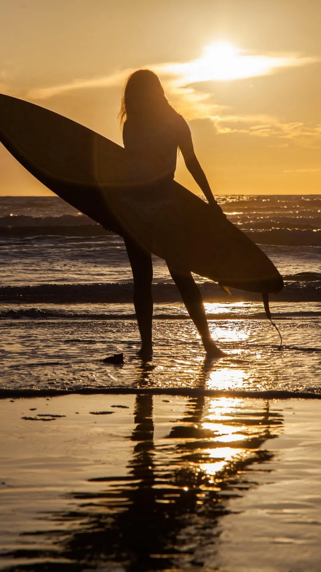 Silhouette of a Surfer Woman Walking Along Beach at Sunset
