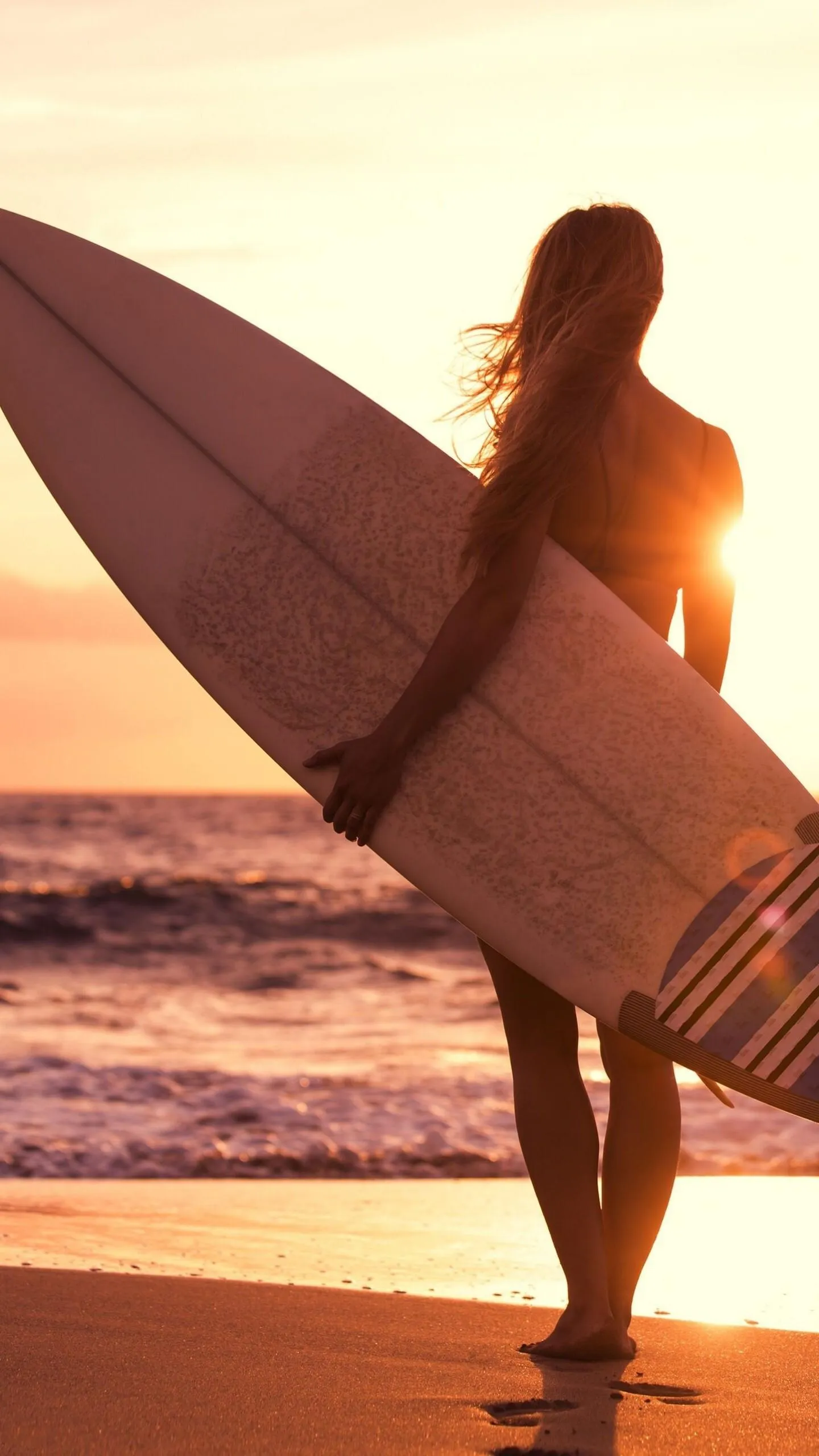 Silhouette of a Woman with a Surfboard on a Beach at Sunset