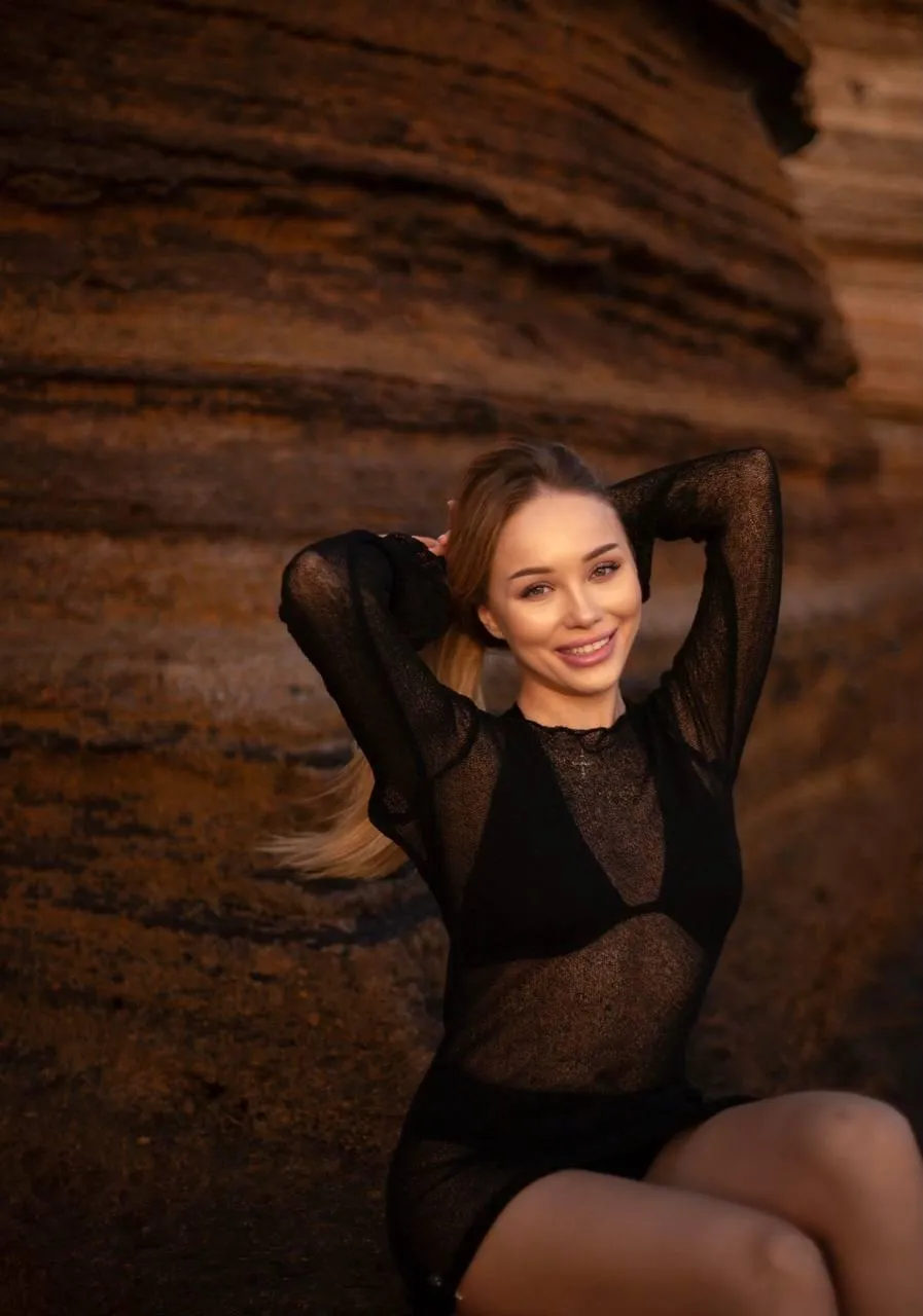 Smiling woman in a sheer black dress near a rocky background