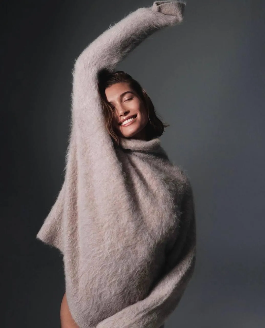 Smiling woman in oversized sweater posing near gray backdrop