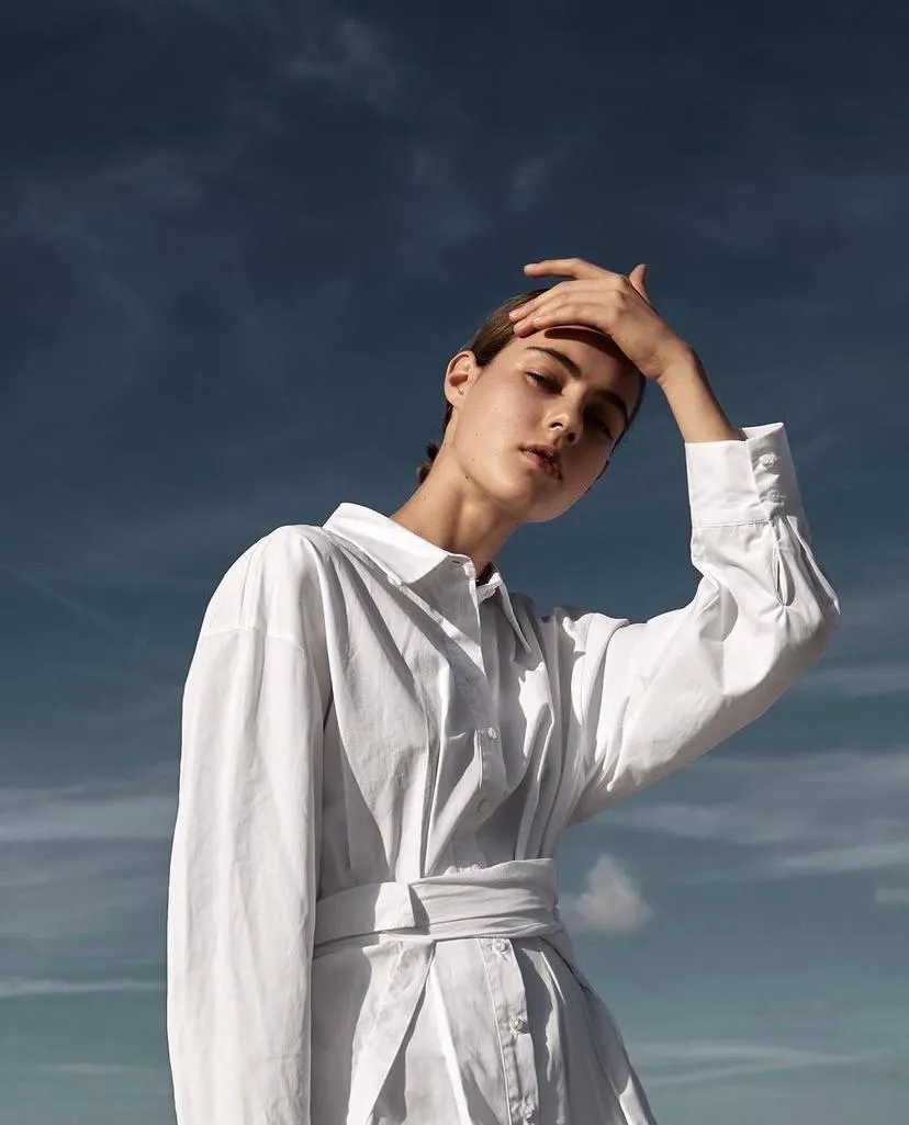 Stylish man in a white outfit standing under a cloudy sky