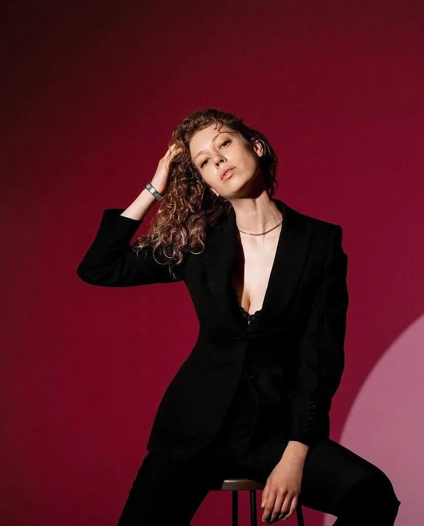 Stylish woman in a black blazer sitting on a stool in studio