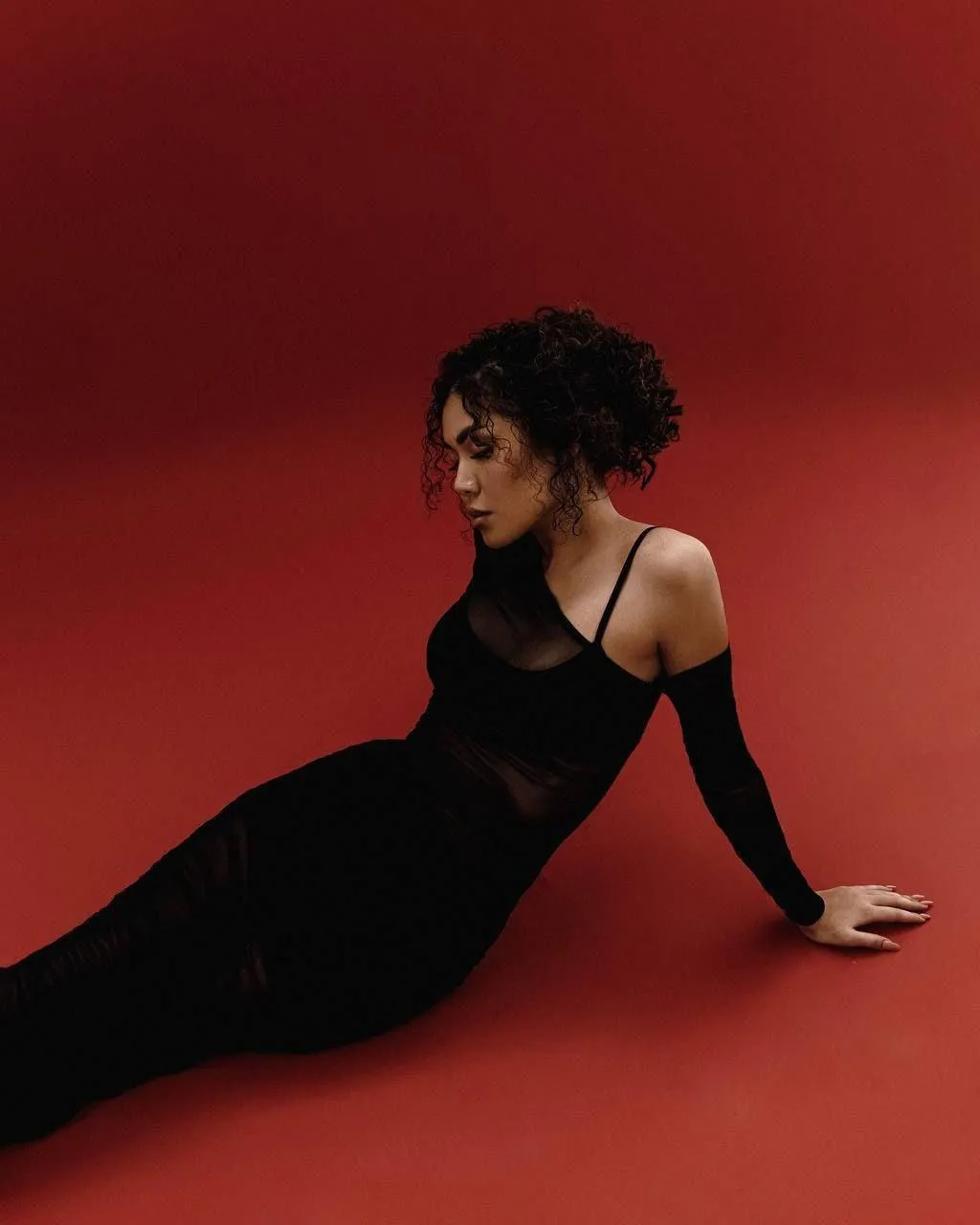 Stylish woman in a black outfit sitting on a red backdrop