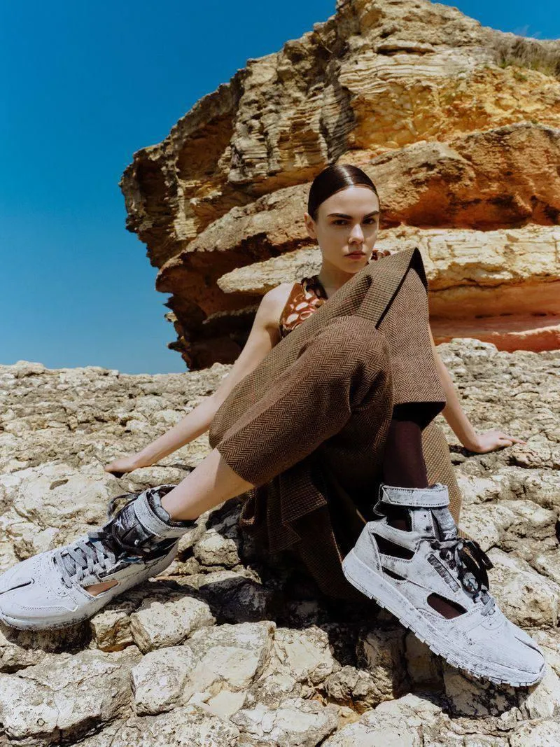 Stylish Woman Poses on Rocky Terrain in White Sneakers Image