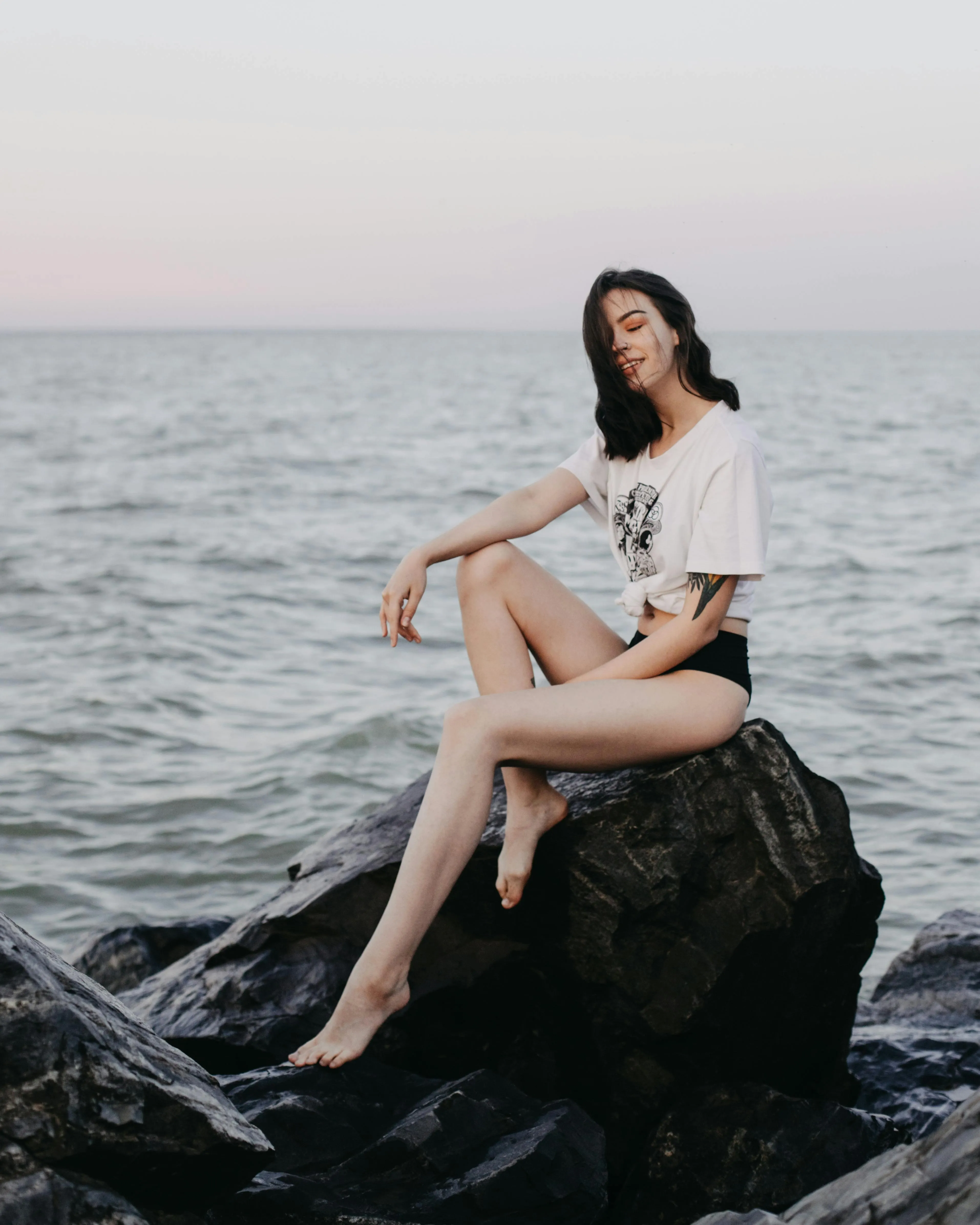 Stylish Woman Sitting on Rock Surrounded by Calm Sea Water
