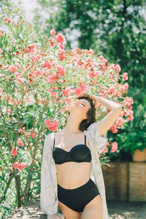 Summer photo of a woman in a black bikini near pink flowers