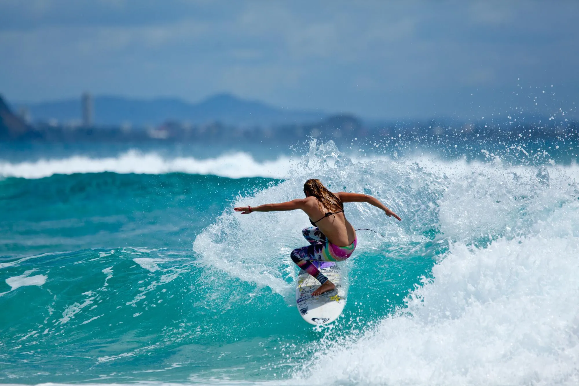Surfer Riding Wave with a Mountainous Coast in the Distance