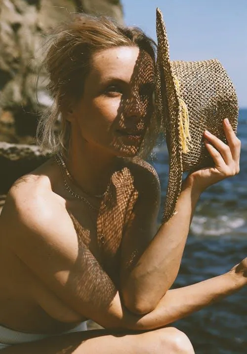 Topless woman sitting near the rock hiding face with a hat