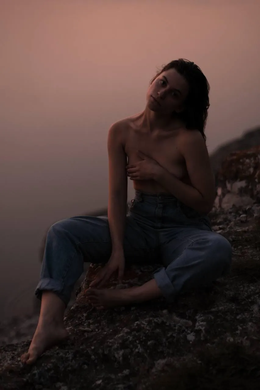 Topless woman sitting on the rocky cliff in the dim sunlit
