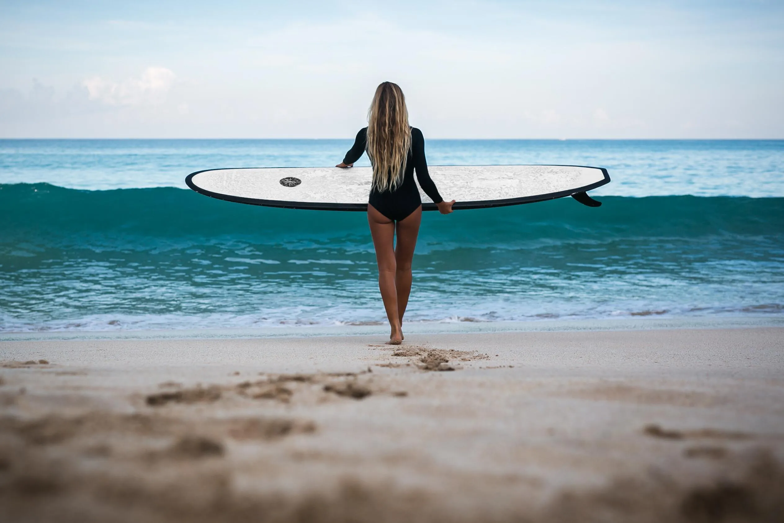 Woman Carrying a Surfboard Walks Toward the Ocean Wallpaper