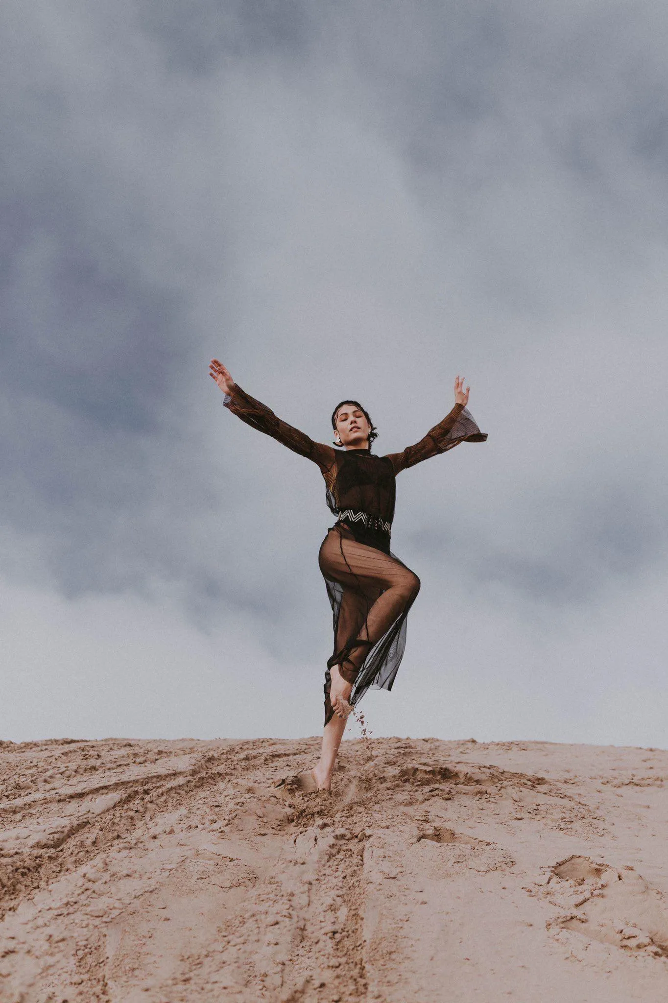 Woman Dancing Freely on a Sand Dune Against a Cloudy Sky