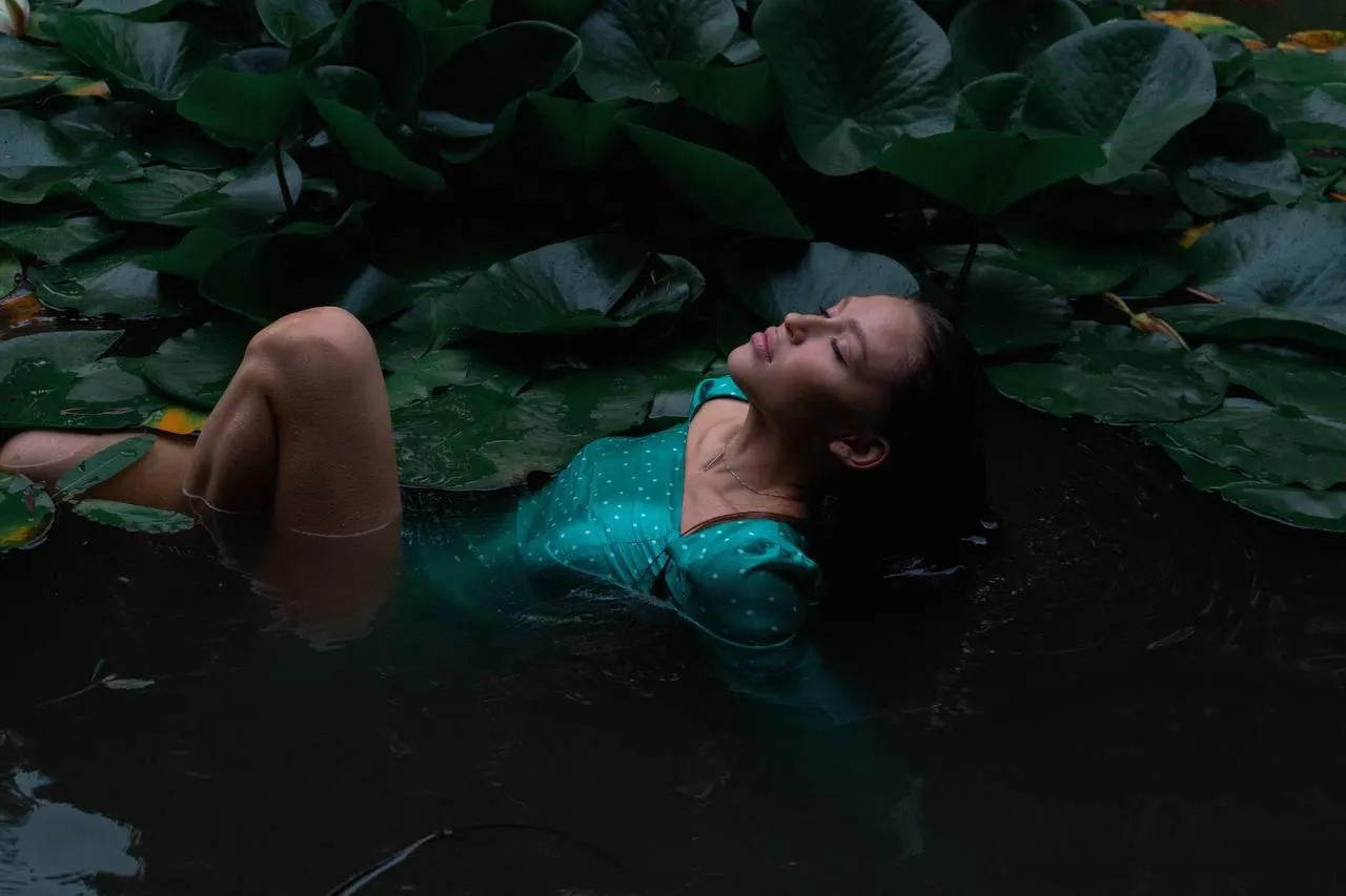 Woman floating peacefully in dark green water with leaves