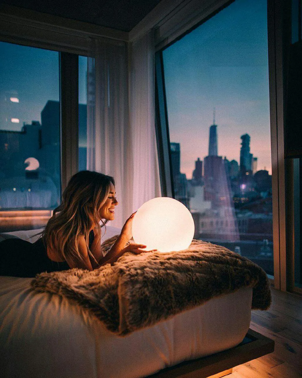 Woman Illuminated by a Warm Lamp Gazes Out City Window Image