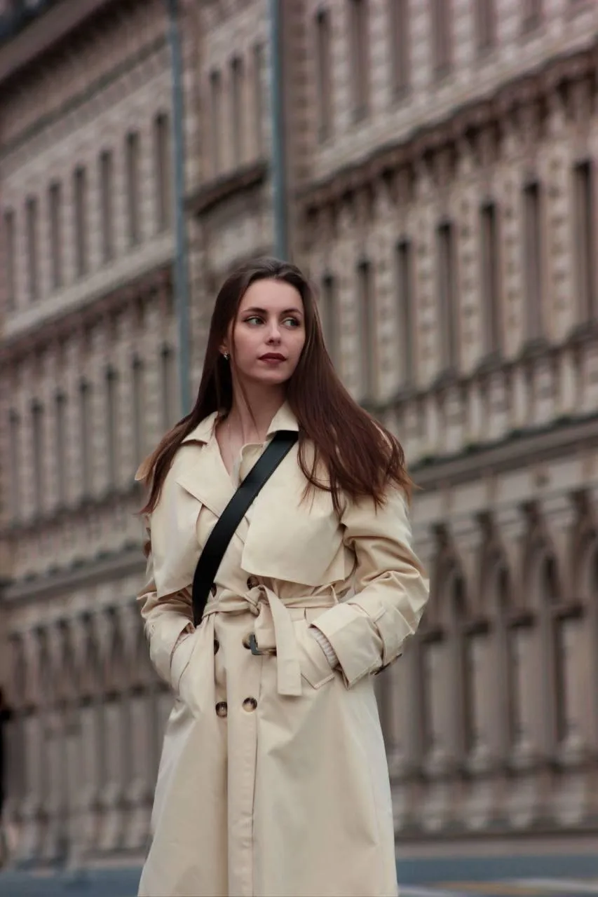 Woman in a beige coat standing near the historic buildings