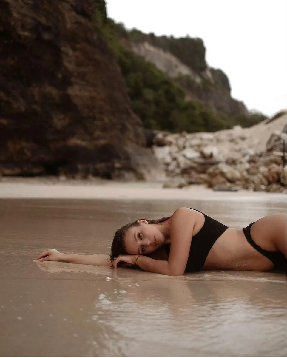 Woman in a black bikini lying on the beach by rocky cliffs