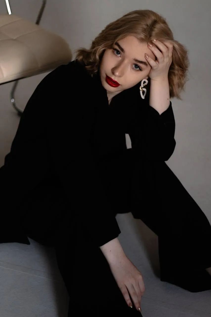 woman in a black blazer sitting on a chair hand on her head