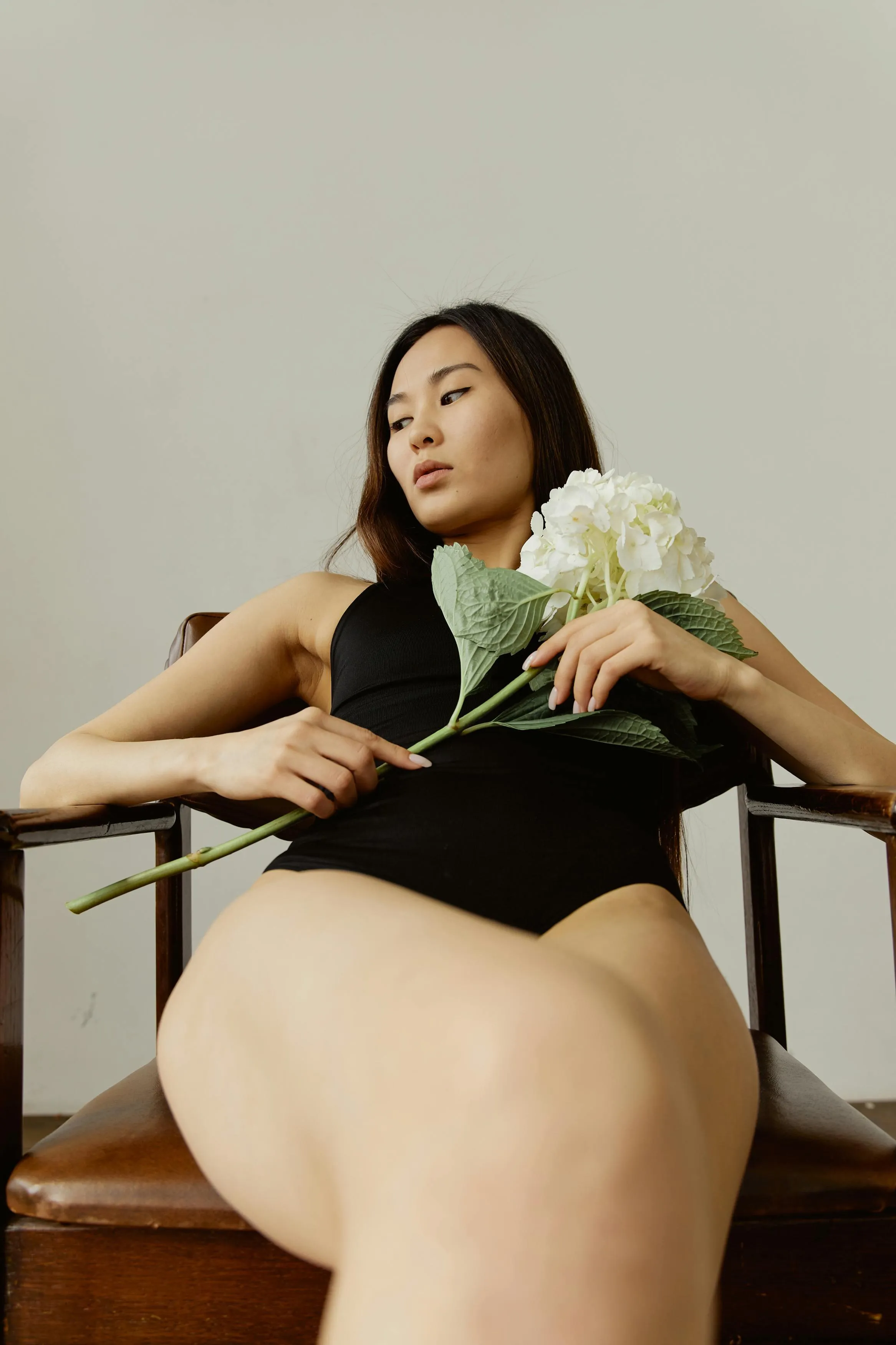 Woman in a Black Bodysuit Holding Flowers in a Wooden Chair