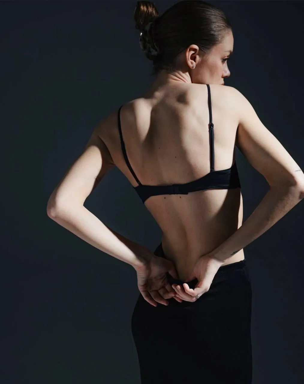 Woman in a black bra fixing dress with dark moody background