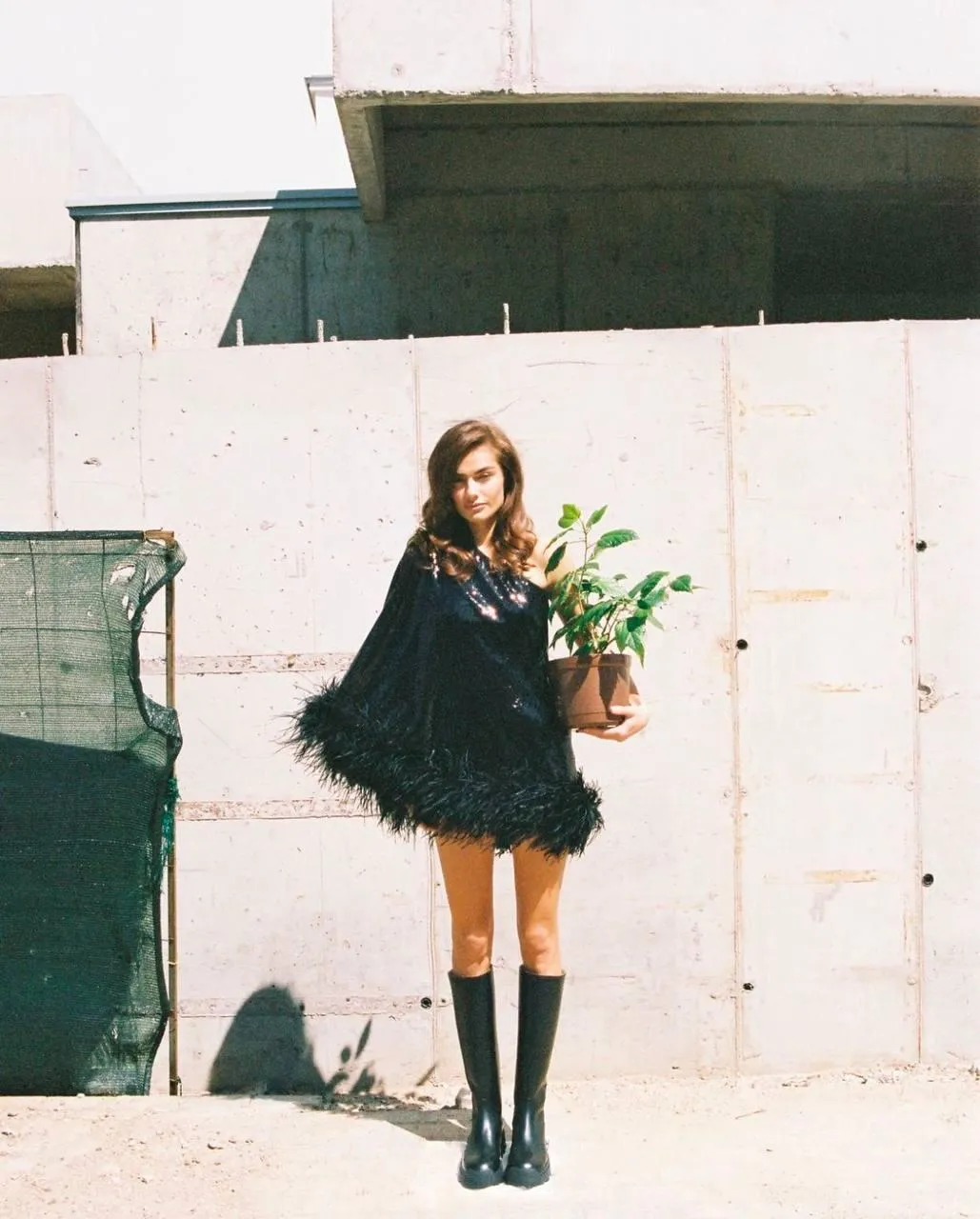 Woman in a Black Dress Holding Flowers Near a White Wall