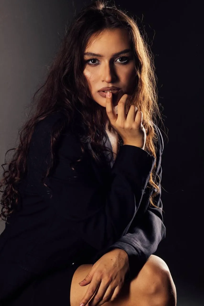 Woman in a black dress with curly hair looking at the camera