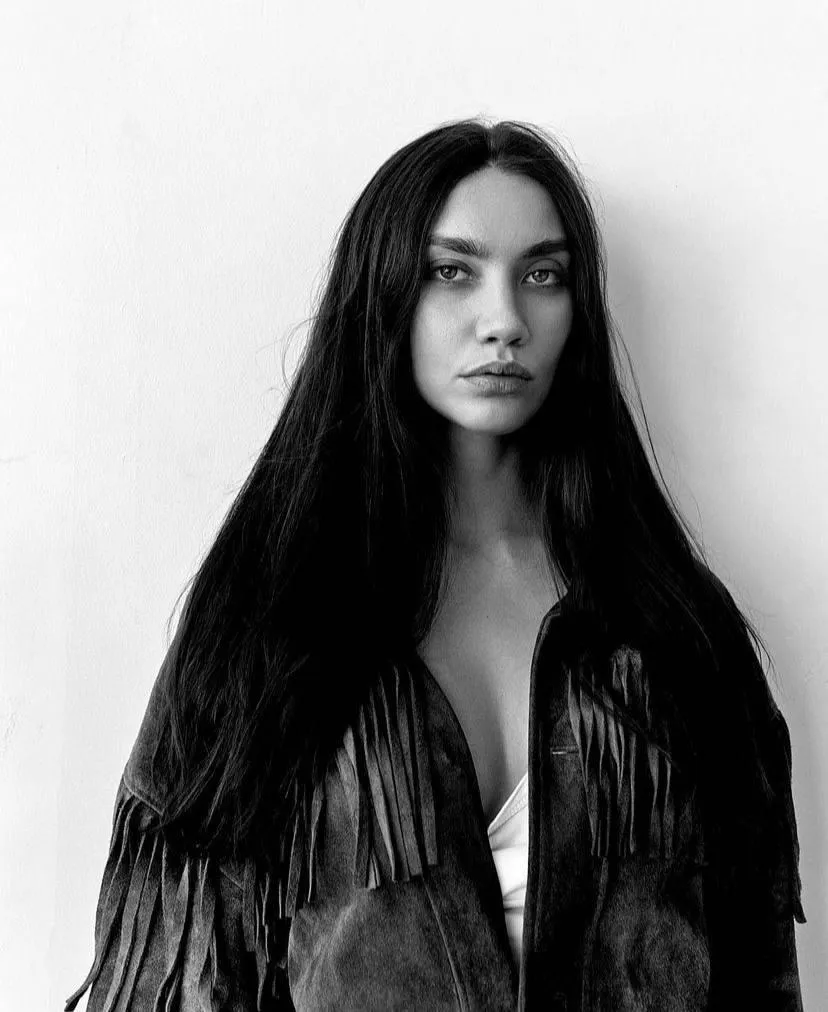 Woman in a black fringe jacket stares boldly at the camera