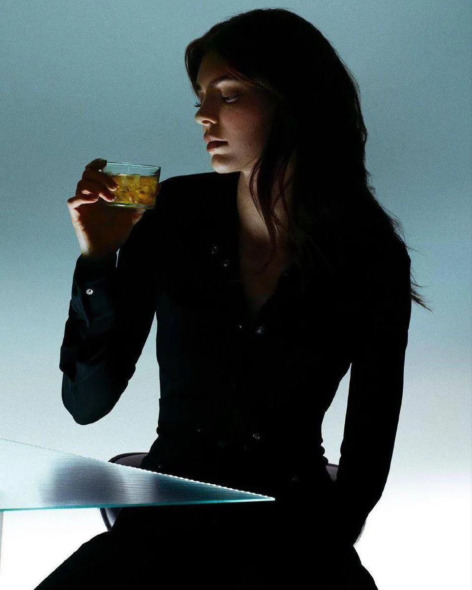 Woman in a Black Outfit Drinking And Gazing Thoughtfully