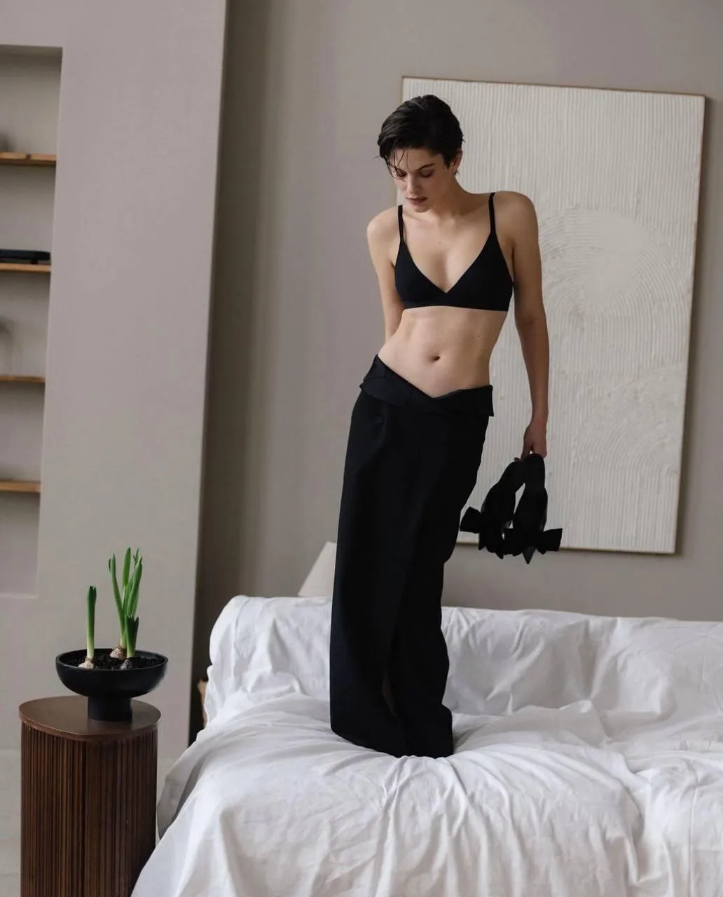 Woman in a black outfit posing by the bed in cozy apartment