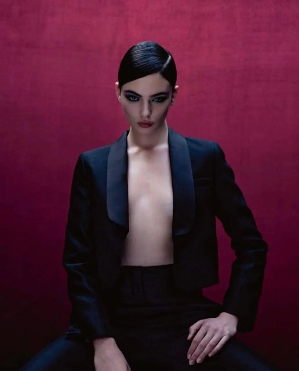 Woman in a black suit posing confidently near red backdrop