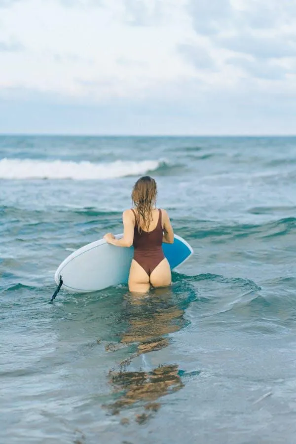 Woman in a bodysuit standing in the sea with a surfboard