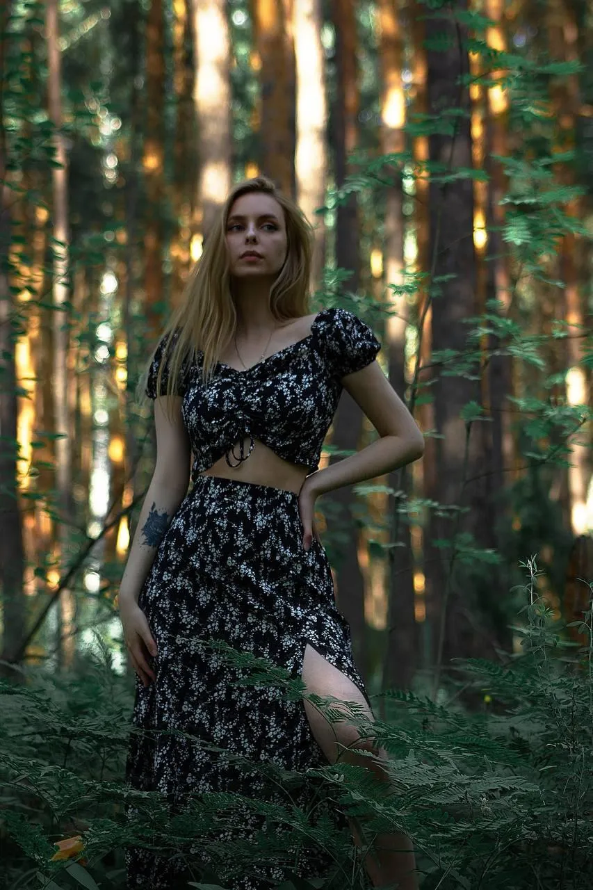 Woman in a Dark Floral Dress Standing in Sunlit Forest Path