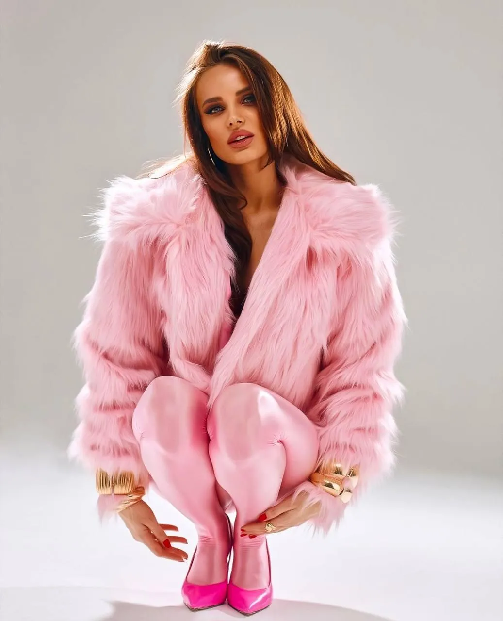 Woman in a fluffy pink coat posing on white studio floor