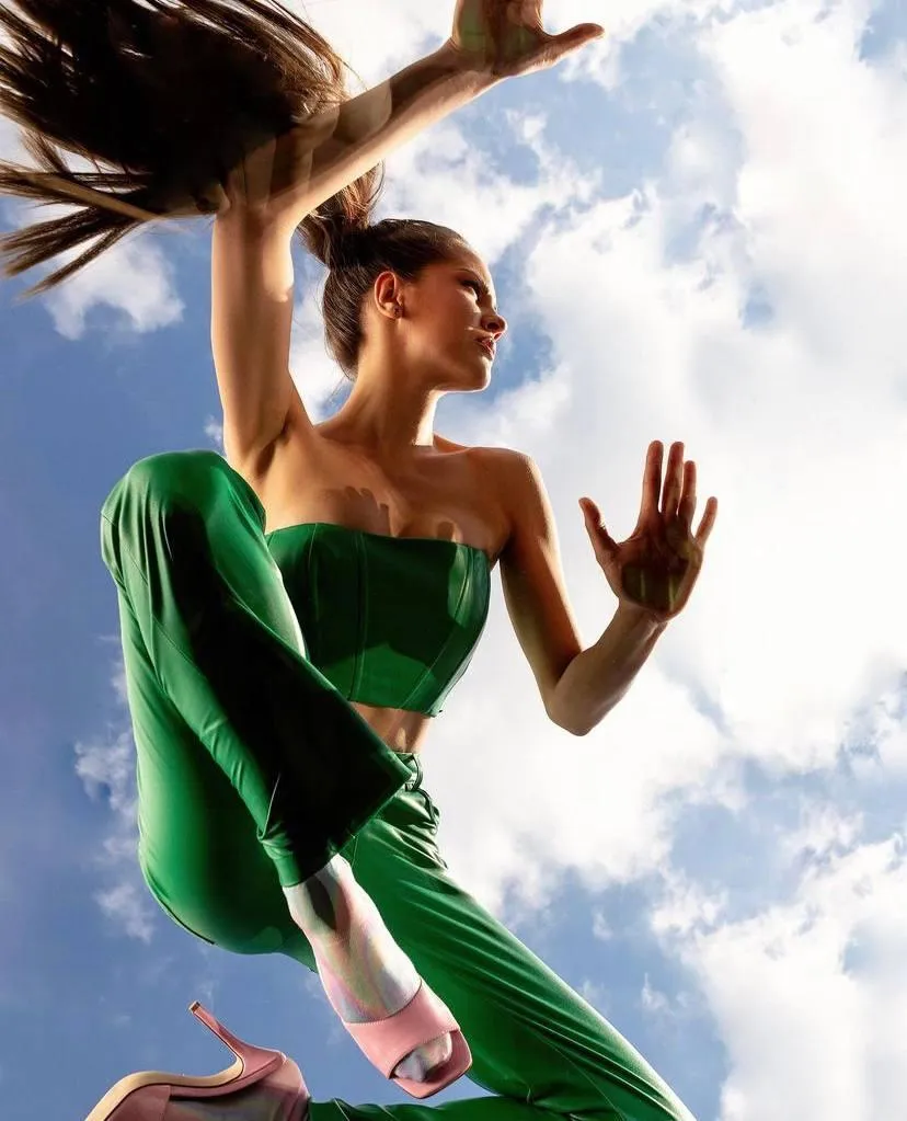 Woman in a green outfit dancing mid air against a blue sky
