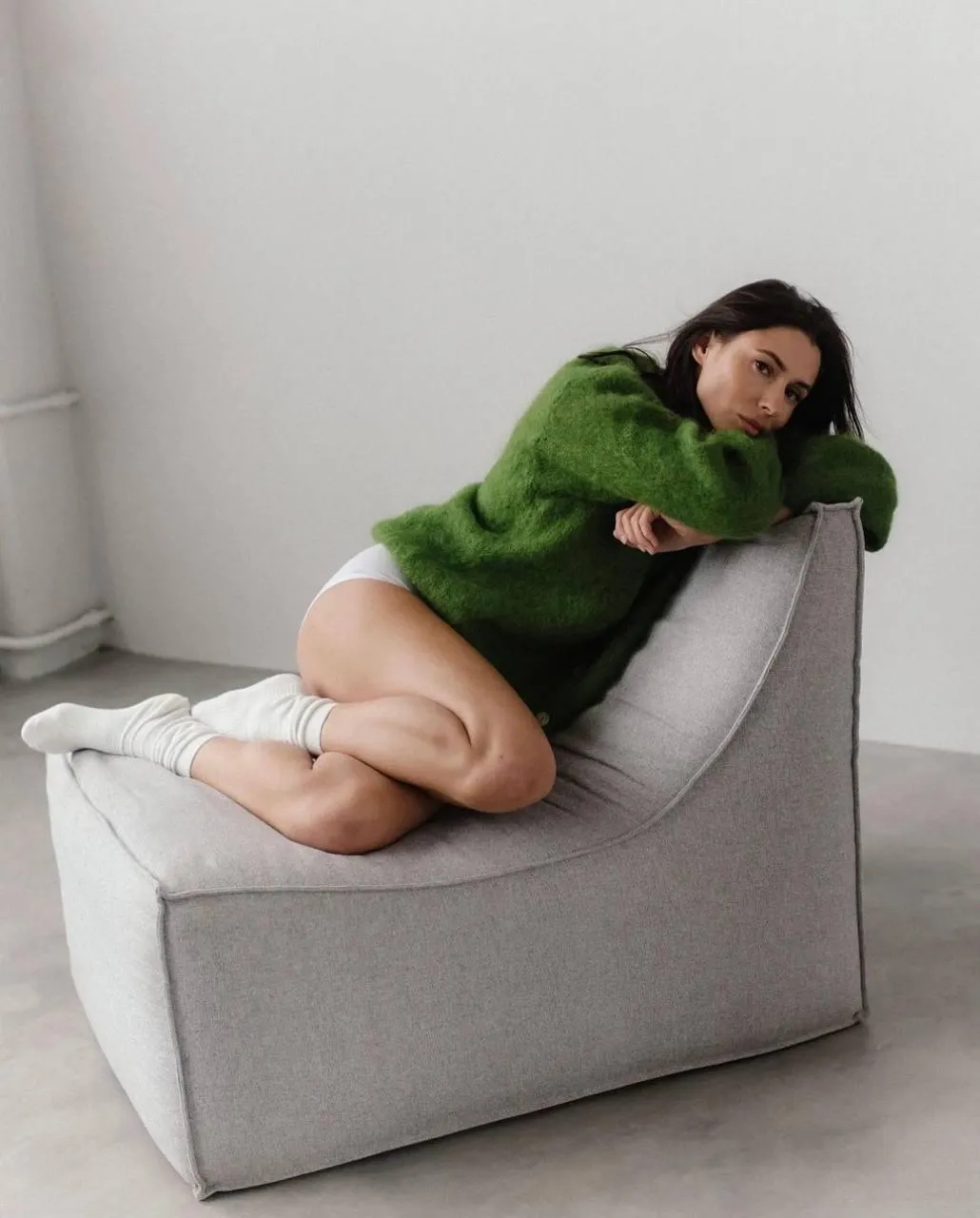 Woman in a Green Sweater Lounging on a Grey Couch Indoors