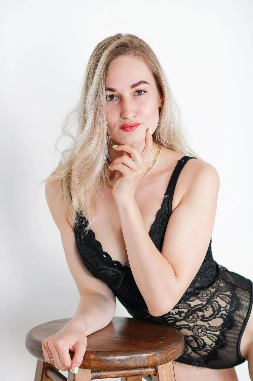 Woman in a Lace Black Outfit Smiling While Seated on a Stool