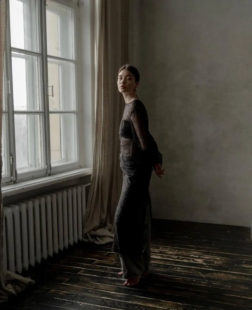 Woman in a Long Black Dress Standing by a Tall Window Light