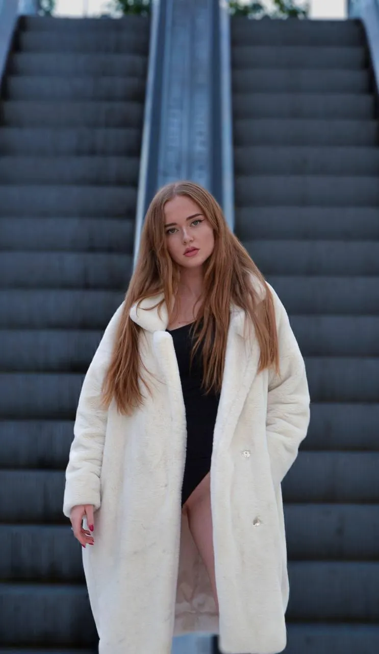 Woman in a long coat standing on an escalator with poise