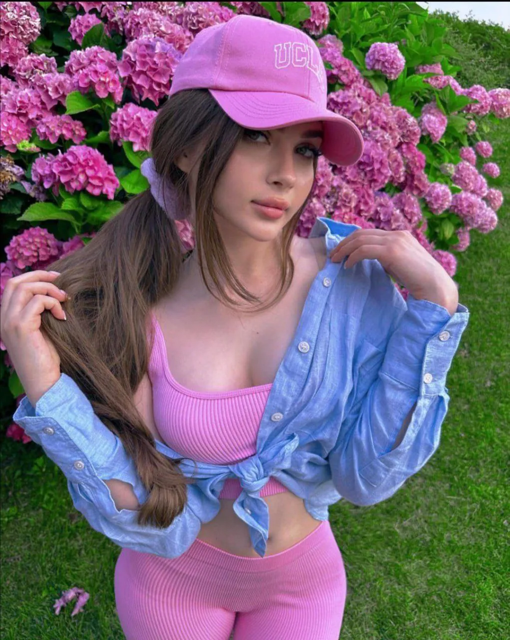 Woman in a Pink Outfit And a Cap Poses by Blooming Flowers