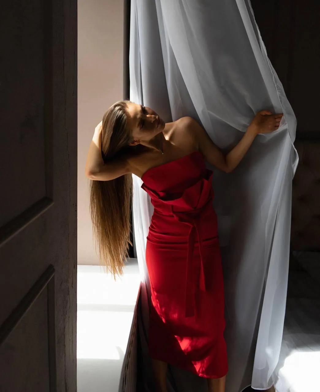 Woman in a red dress peeking out from behind curtains image