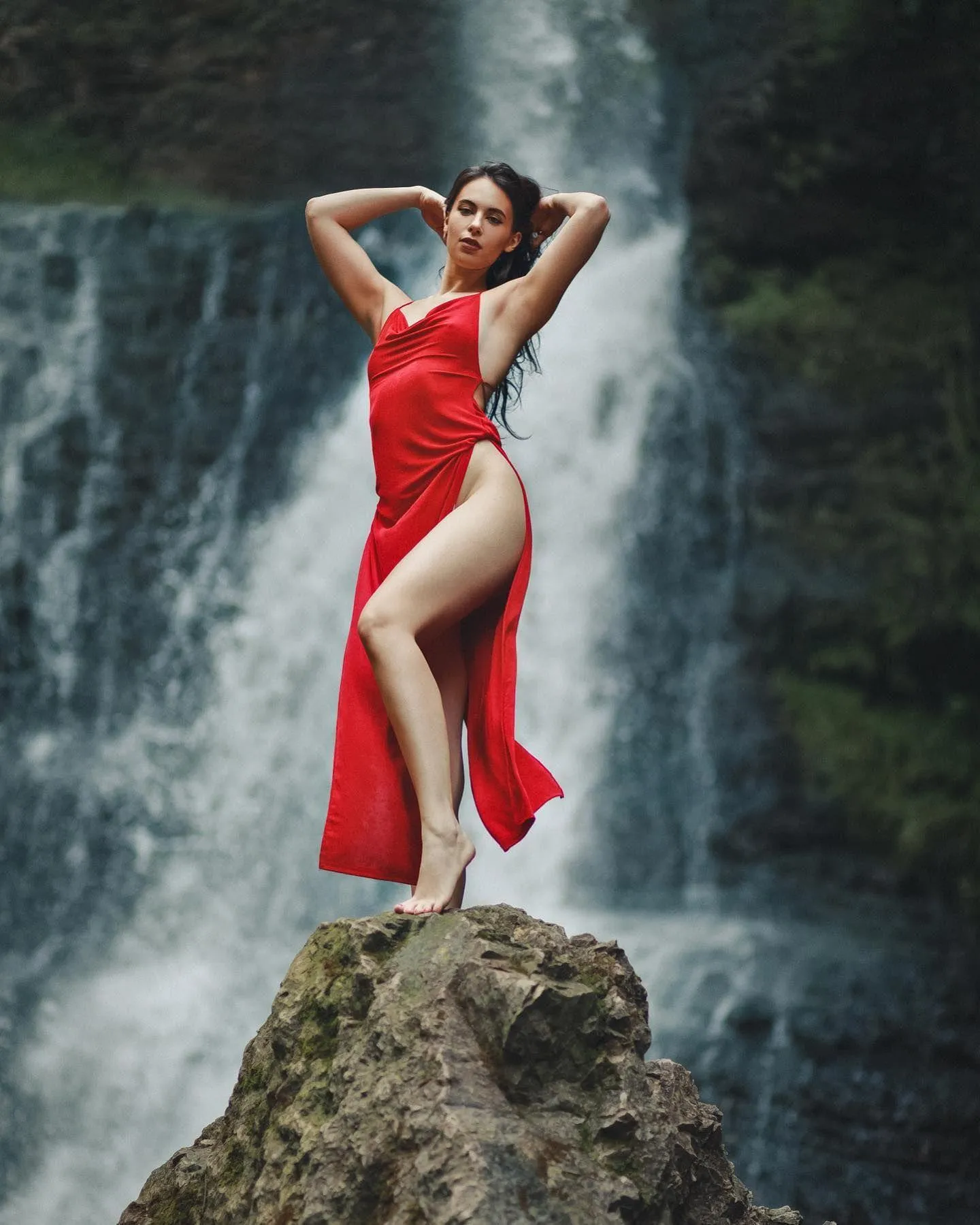 Woman in a Red Dress Poses Confidently Near a Tall Waterfall