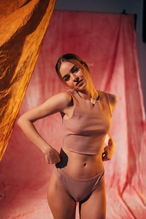 Woman in a skintone dress standing near the red background