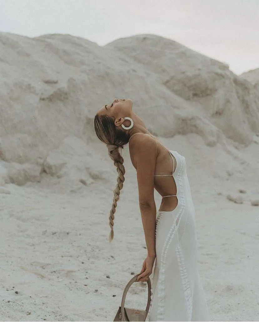 Woman in a white bathing suit bending forward on sandy hill